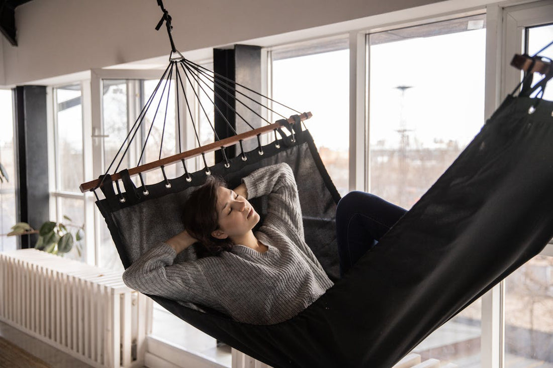 Woman relaxing in an indoor hammock near a window demonstrating hammock sleeping setup