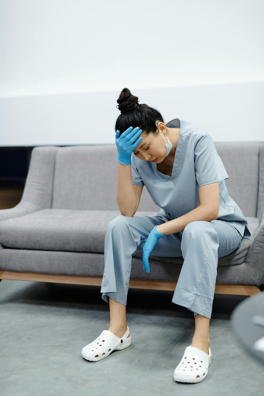 Tired nurse in scrubs sitting on sofa after long hospital shift